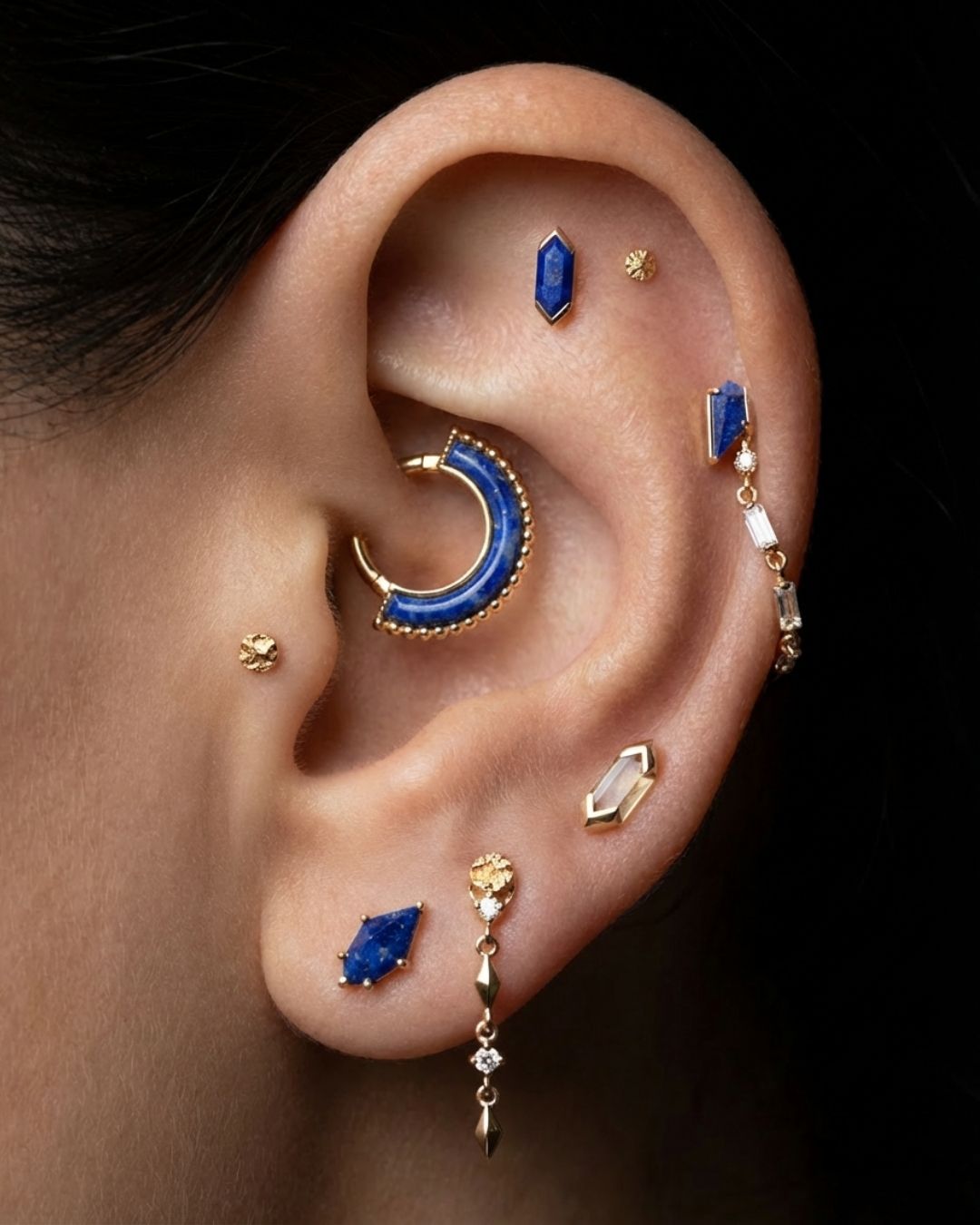 Composición de joyería DLezcano con elementos azules y dorados sobre una oreja